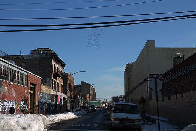 Reed Bmore's sign painter hangs on a telephone wire at Thames and Bogart (Photo by Emilie Ruscoe for Bushwick Daily).