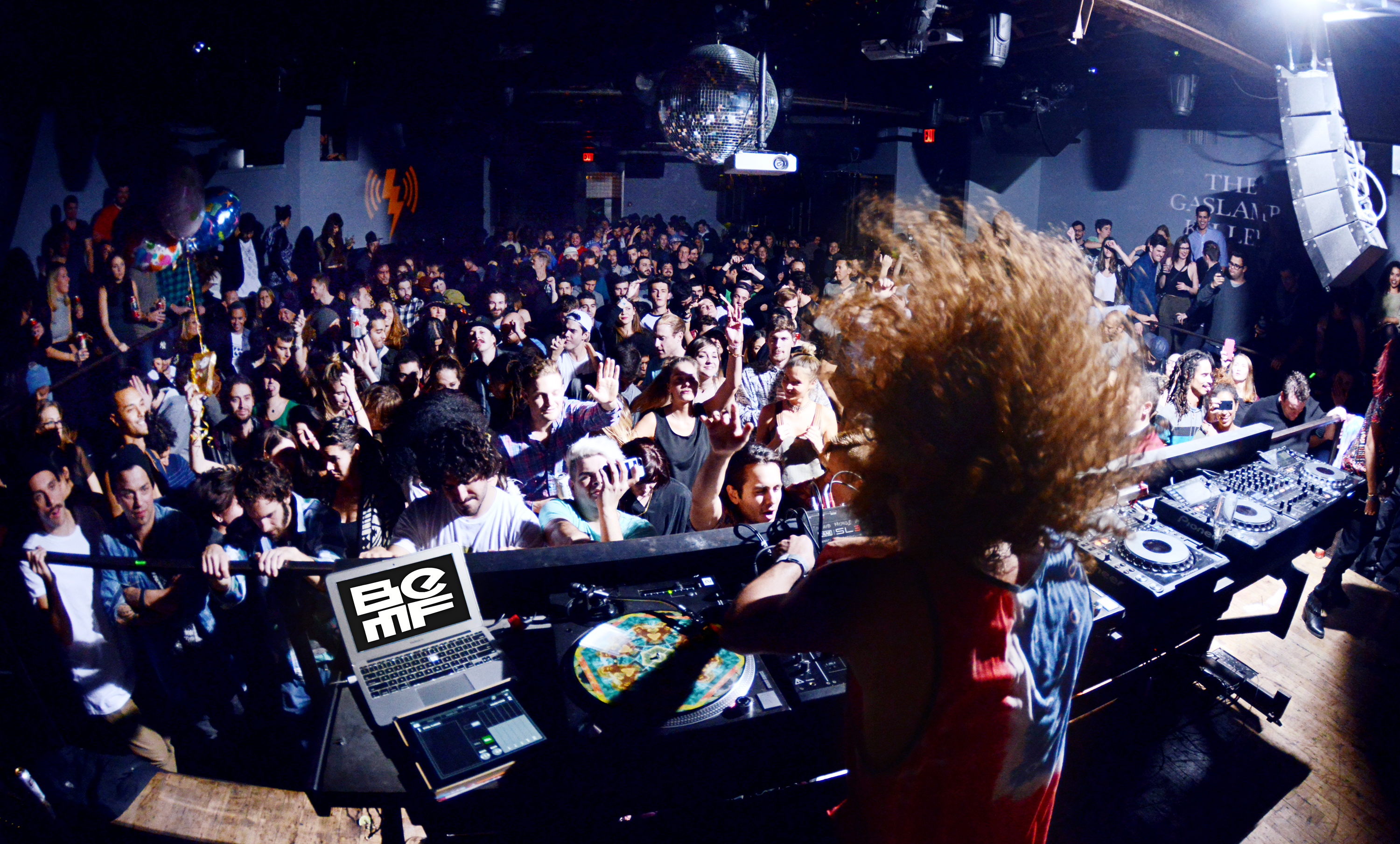DJ performs at BEMF as crowd dances beneath disco ball with BEMF logo visible on laptop