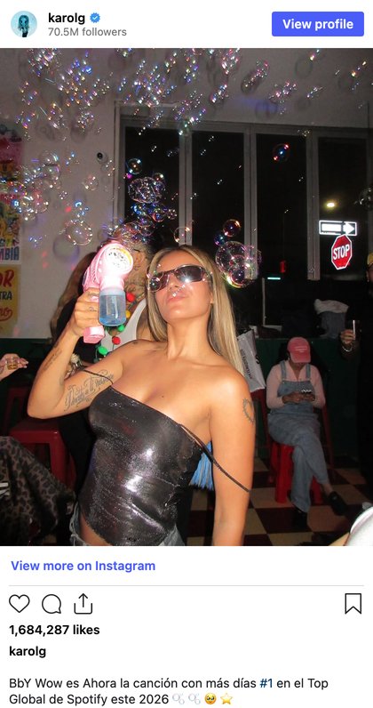 Screenshot of Karol G's Instagram post: she blows bubbles from a pink bubble gun in a bar; nearly 1.7 million likes; caption about BbY Wow on Spotify's Top Global chart.